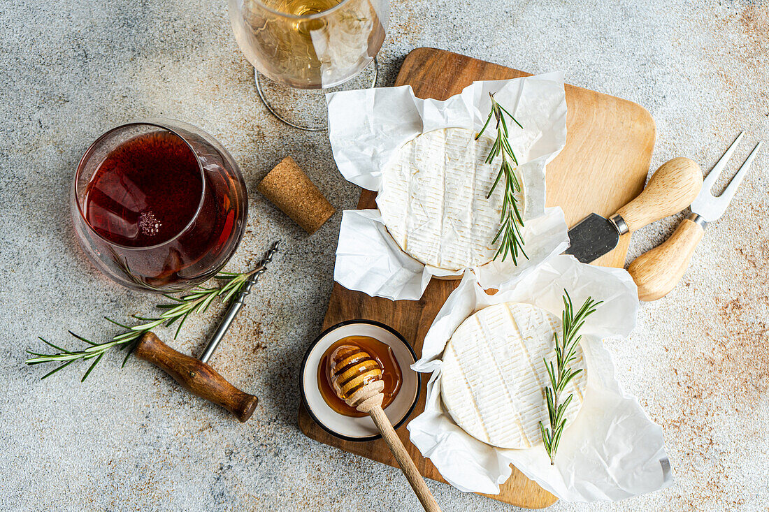 Top view of red and white wine glasses paired with Brie cheese, honey, and rosemary on a wooden board, ideal for a luxurious snack or appetizer.