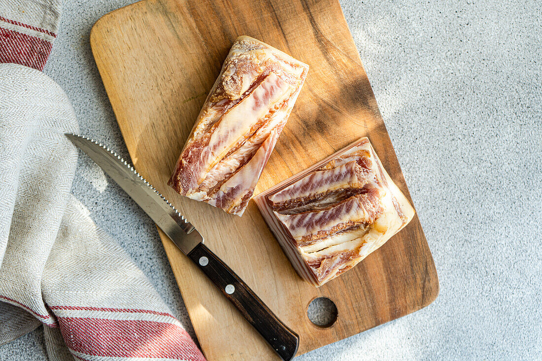 From above rustic scene with a large piece of pork lard and thin slices atop crusty bread, all placed on a wooden cutting board.