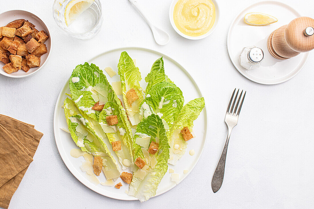 Draufsicht auf einen Caesar-Salat mit knackigem Römersalat, Croutons und gehobeltem Parmesankäse, elegant angerichtet auf einem weißen Hintergrund.