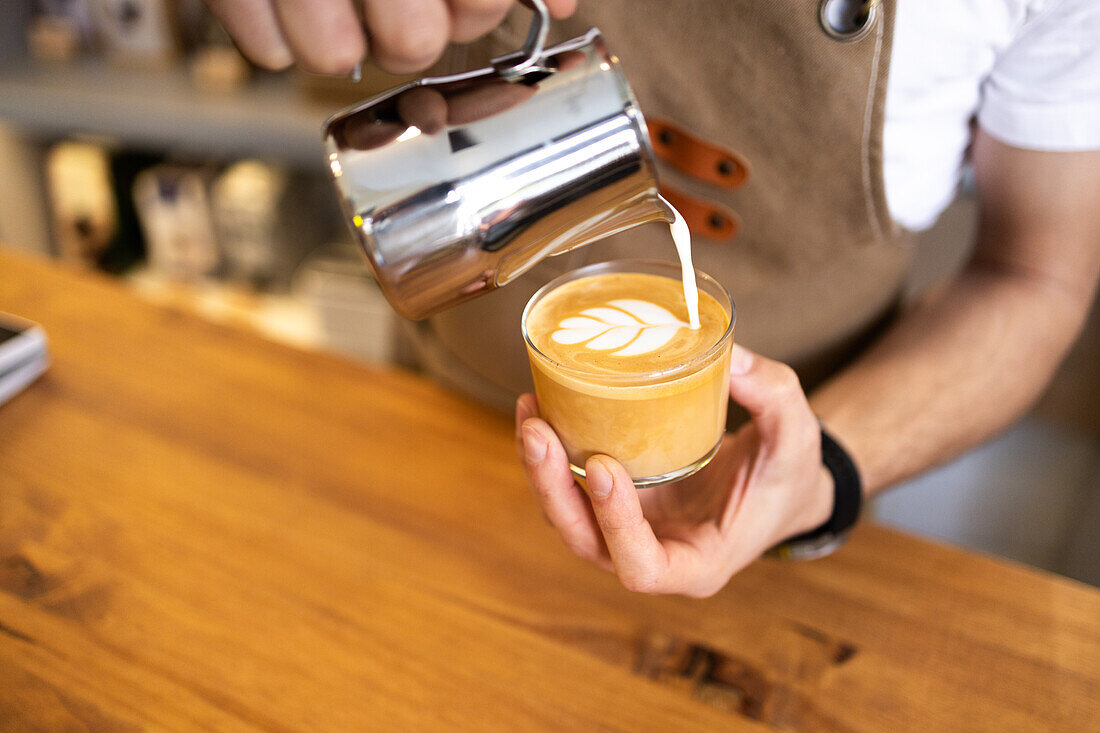 A skilled barista carefully pours steamed milk into a cup of espresso, creating an intricate latte art design.