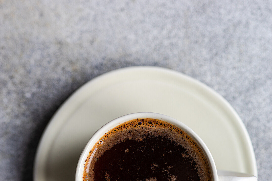 Blick von oben auf einen frisch gebrühten heißen Kaffee in einer weißen Tasse auf einer Untertasse, mit einer schaumigen Oberfläche, perfekt für einen morgendlichen Energieschub.