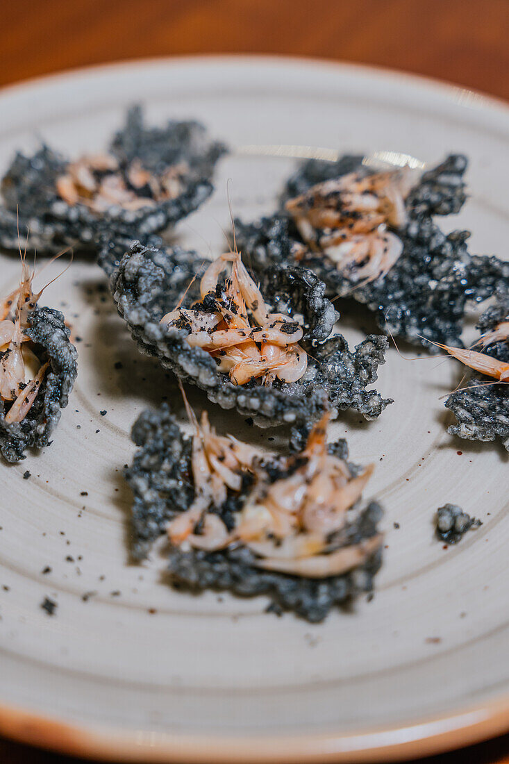 Exquisite Holzkohle-Tempura-Garnelen, garniert mit zarten Kräutern auf einem Keramikteller, der die gehobene Gastronomie verkörpert