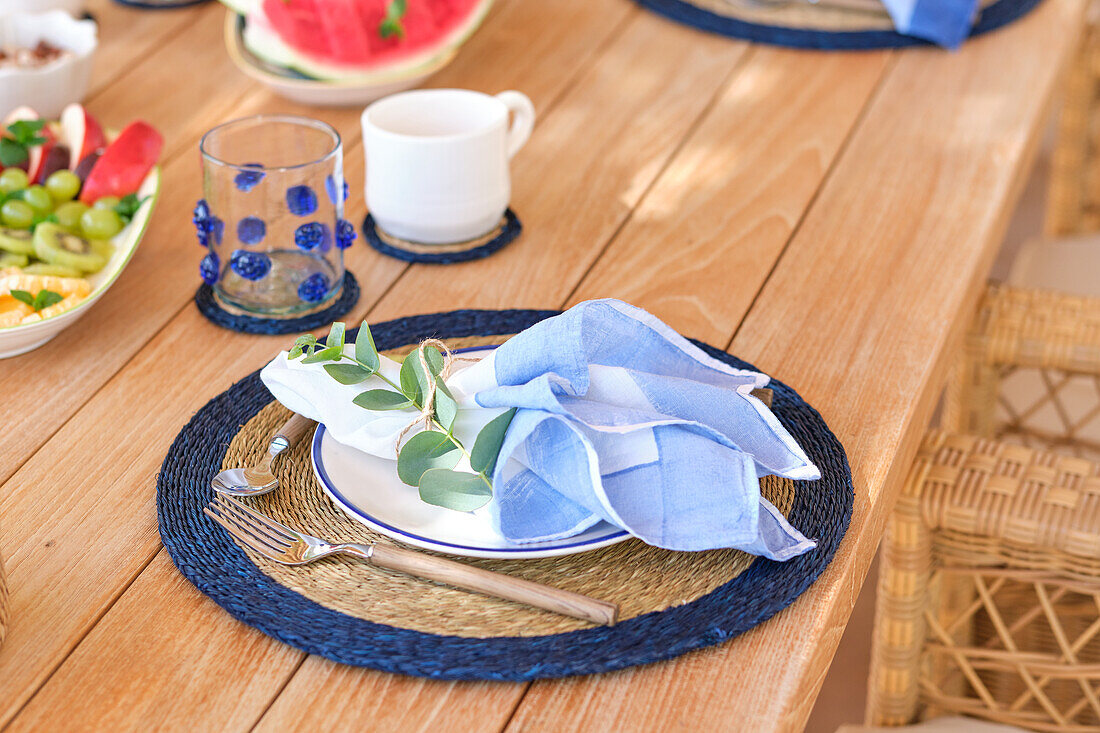 A close-up view of a breakfast table on a terrace, showcasing an elegant plate and cutlery arrangement with a touch of greenery