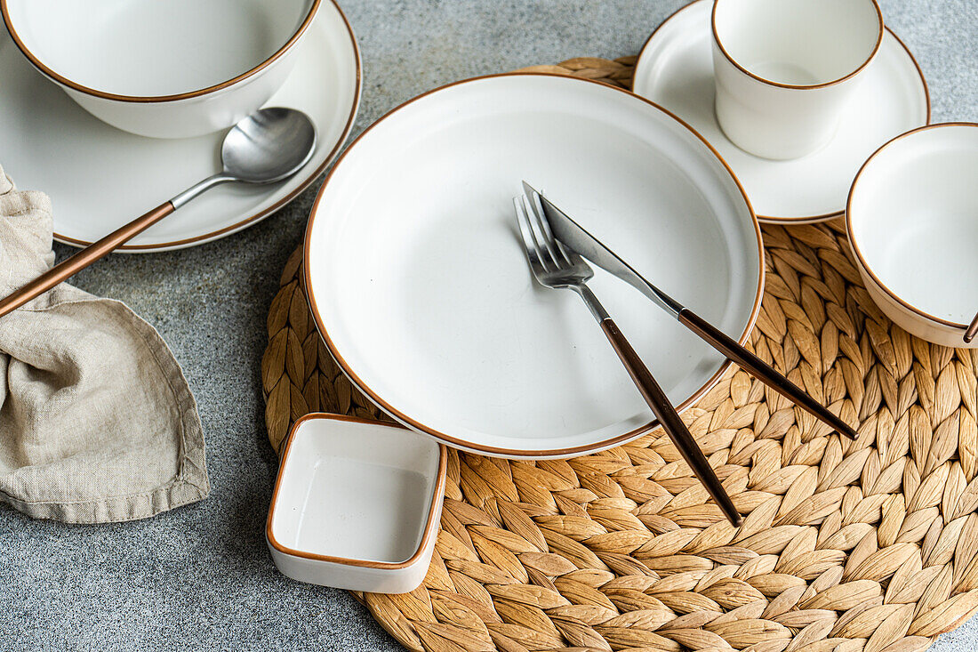 Top view of a stylish table setting featuring bright ceramic dinnerware, cutlery, and a woven placemat, ready for a refined meal.