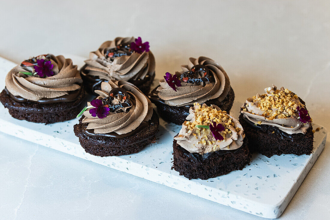 High angle of vegan chocolate sponge cakes with whipped cream and flower decorations served on cutting board on table in bakery