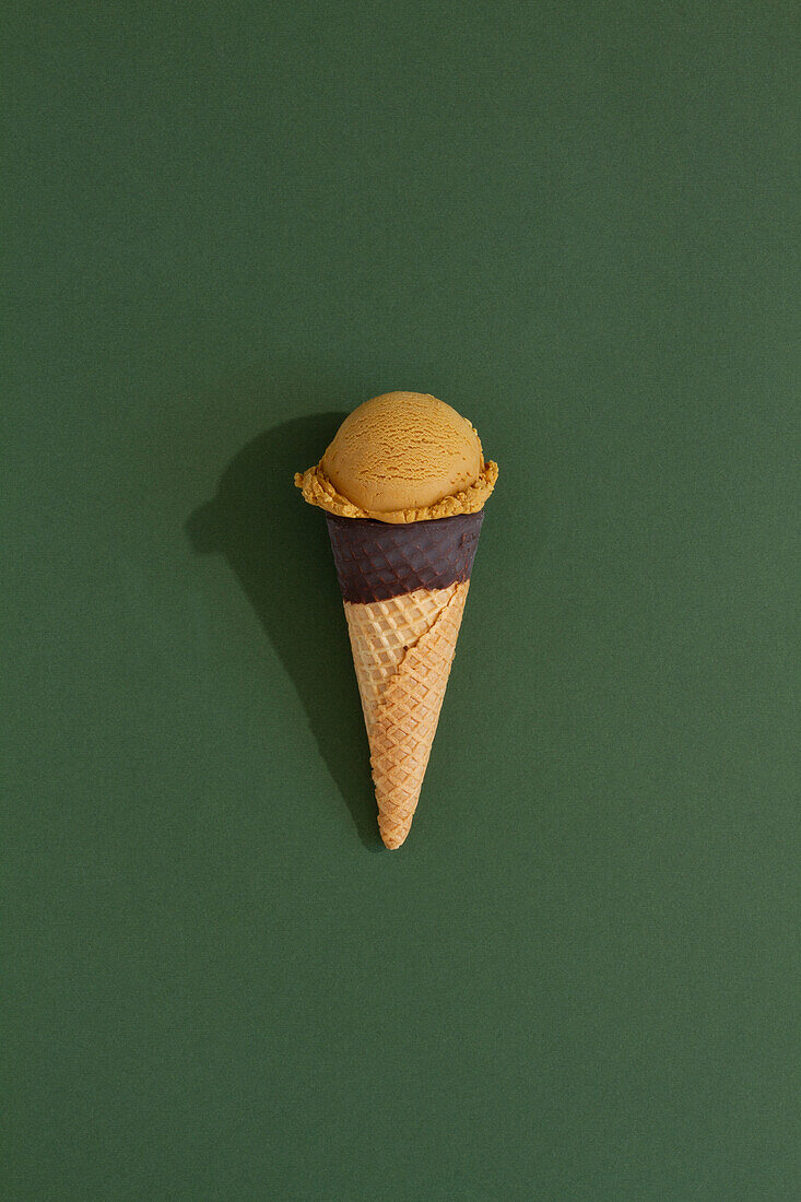 A vibrant pistachio ice cream scoop sits atop a classic waffle cone against a green background, casting a playful shadow