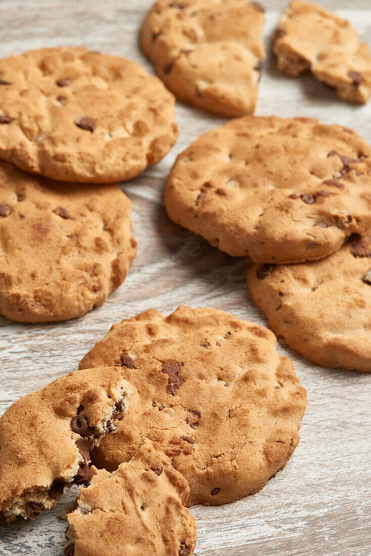 Artisanal chocolate chip cookies with a golden hue, displayed invitingly on a textured wooden surface, some with a bite taken out