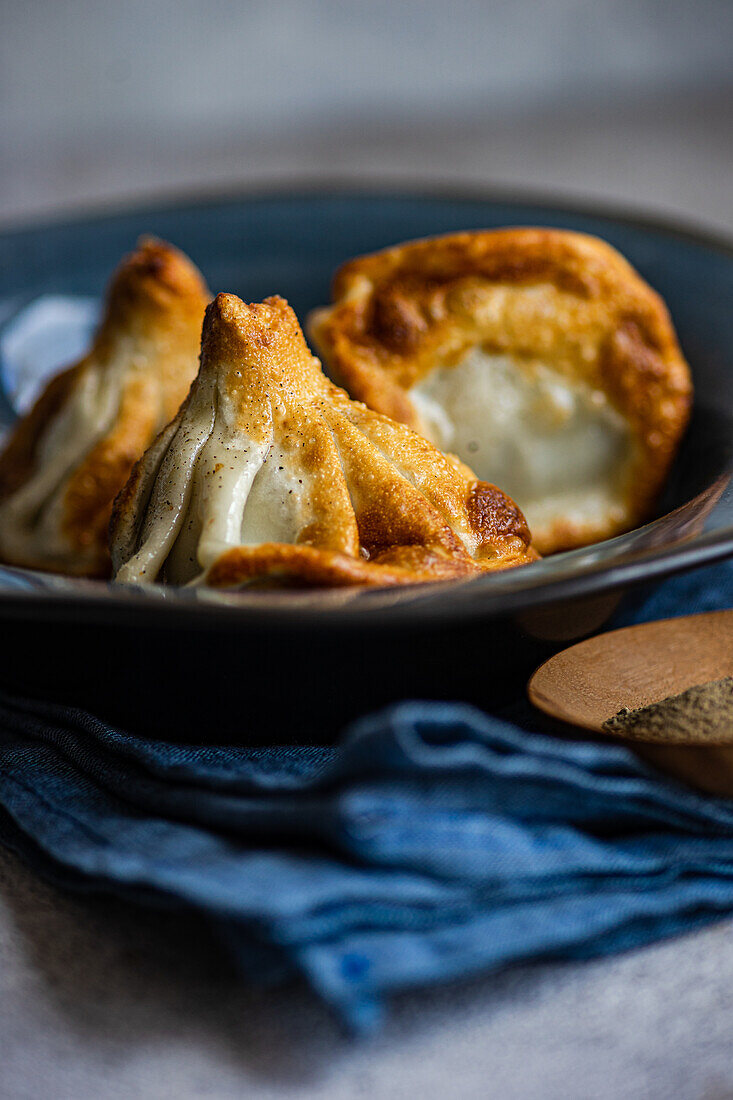 A close-up shot of freshly cooked traditional Georgian Khinkali, served in a deep blue bowl, highlighting the textured dough and steamy filling