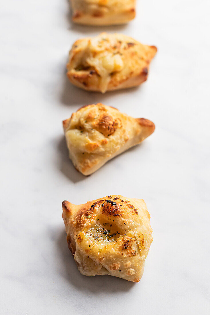 Freshly baked garlic bread knots, seasoned with herbs and cheese, perfectly golden brown and placed neatly on a white surface.