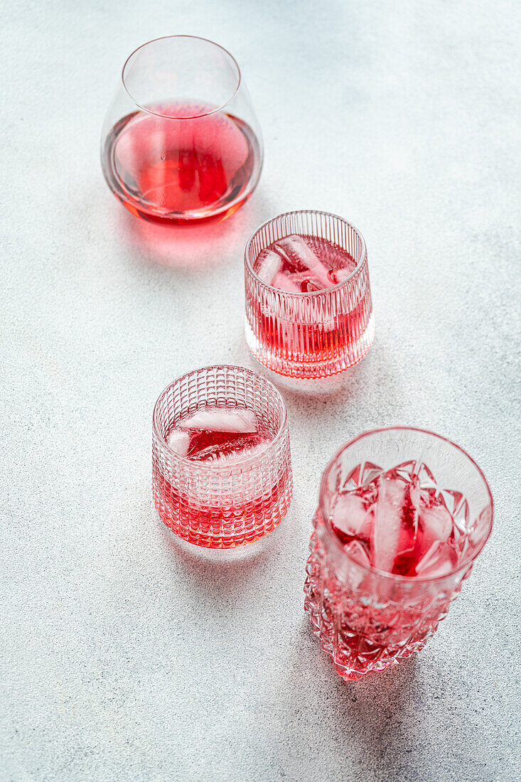 Draufsicht auf elegante Gläser, die mit einem erfrischenden Kirsch-Wodka-Tonic-Cocktail gefüllt sind, begleitet von Eiswürfeln, die auf einer strukturierten Oberfläche stehen.