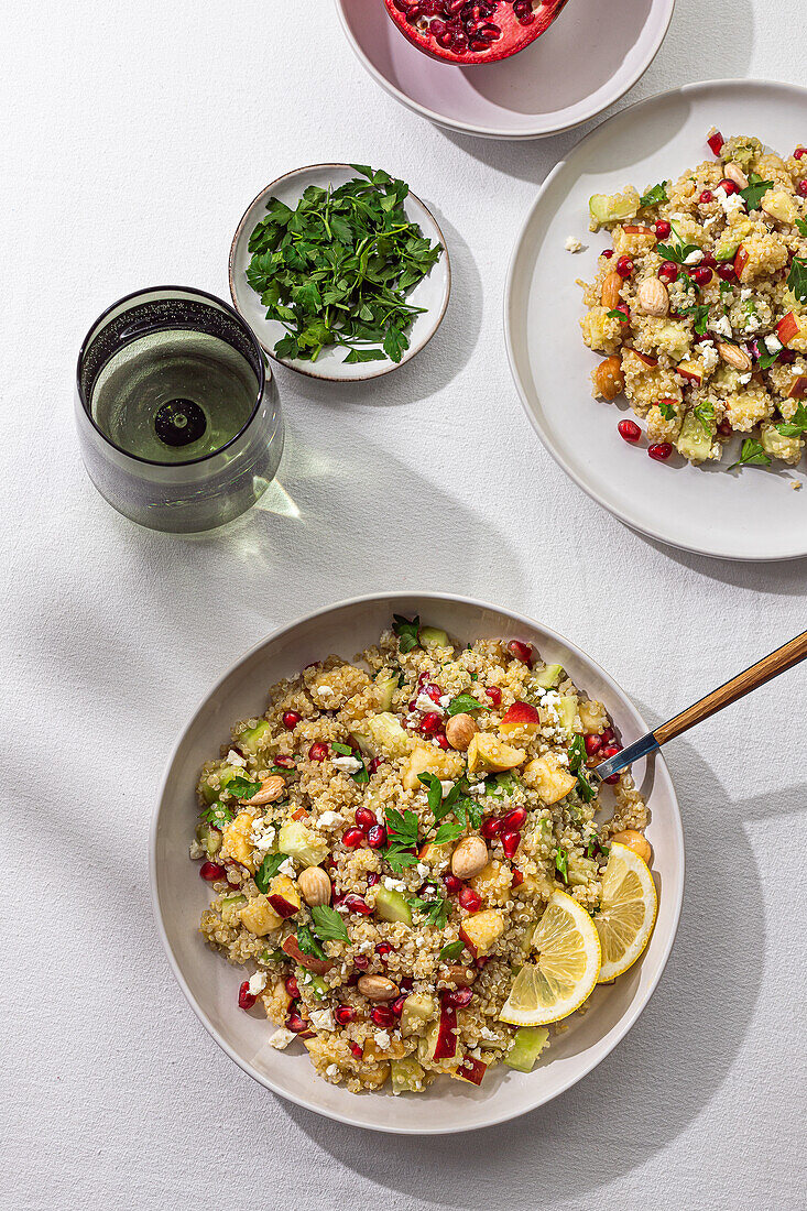 A vibrant top view of homemade curry quinoa salad garnished with pomegranate seeds, lemon slices, and fresh parsley on the side.