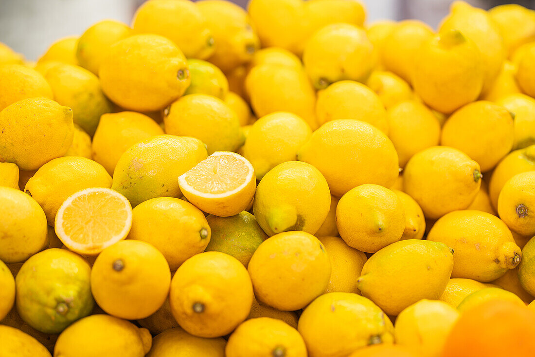 Ein leuchtender Haufen frischer, reifer Zitronen mit einer einzelnen halbierten Zitrone, die ihr saftiges Inneres offenbart