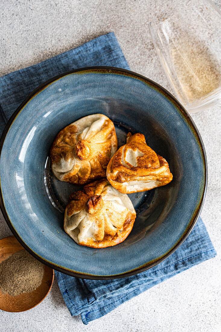 Traditional Georgian dumplings, khinkali, are perfectly cooked and served in a stylized blue ceramic bowl atop a denim cloth, with a subtle backdrop of spices