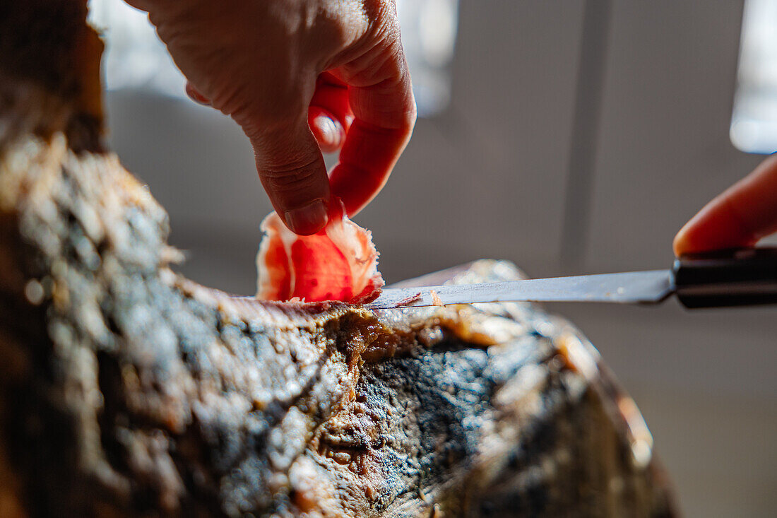 A detailed close-up captures a hand carefully slicing a piece of Serrano Ham from a seasoned leg The texture of the meat and the precision of the cut highlight traditional Spanish cuisine