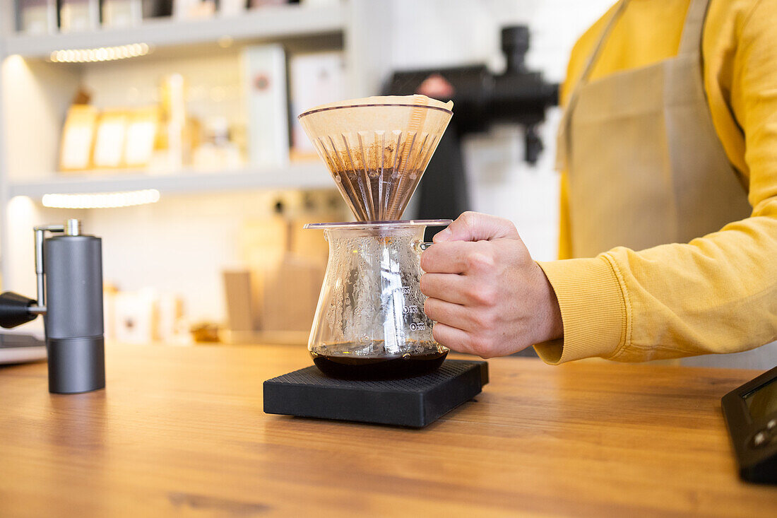 A close-up of a barista's hand pouring hot water through a coffee filter into a carafe at a stylish coffee shop.