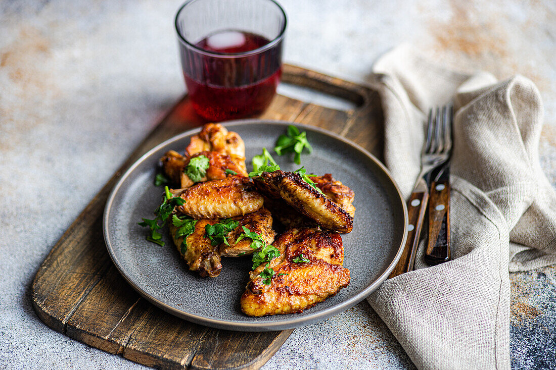 Crispy roasted chicken wings seasoned with spicy sauce and garnished with fresh coriander, accompanied by a cherry cocktail in a glass, presented on a rustic plate.