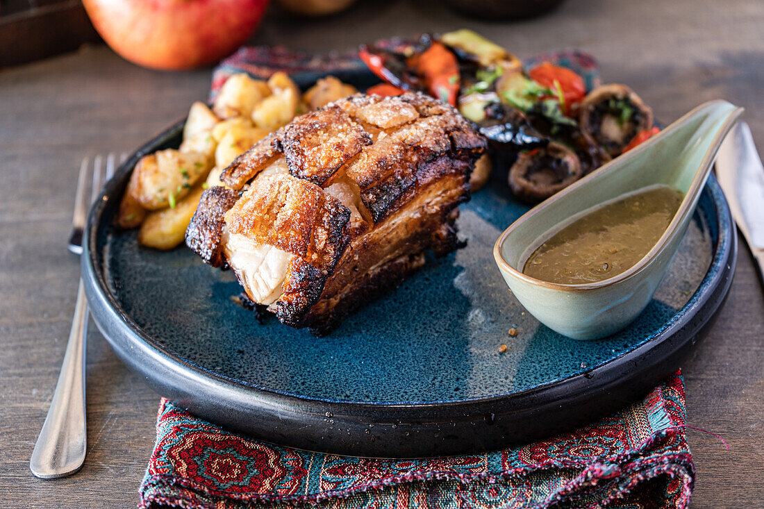 Schweinebraten, glasiert mit einer reichhaltigen Honigsauce, begleitet von einem bunten Salat aus gegrilltem Gemüse und Kartoffeln, serviert auf einem blauen Keramikteller in rustikaler Umgebung