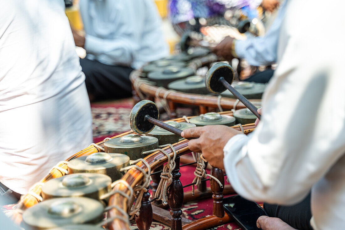 Nahaufnahme der Hände einer unkenntlich gemachten Person, die während einer kulturellen Zeremonie traditionelle thailändische Musikinstrumente spielt und die Kunst der thailändischen Musik vorführt.