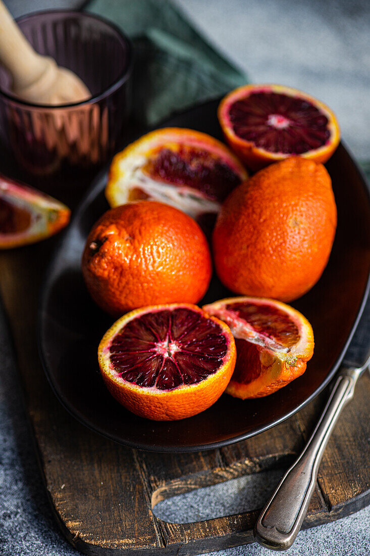 Vibrant blood oranges, some sliced, arranged on a dark rustic plate alongside vintage cutlery, evoking a fresh and natural feel