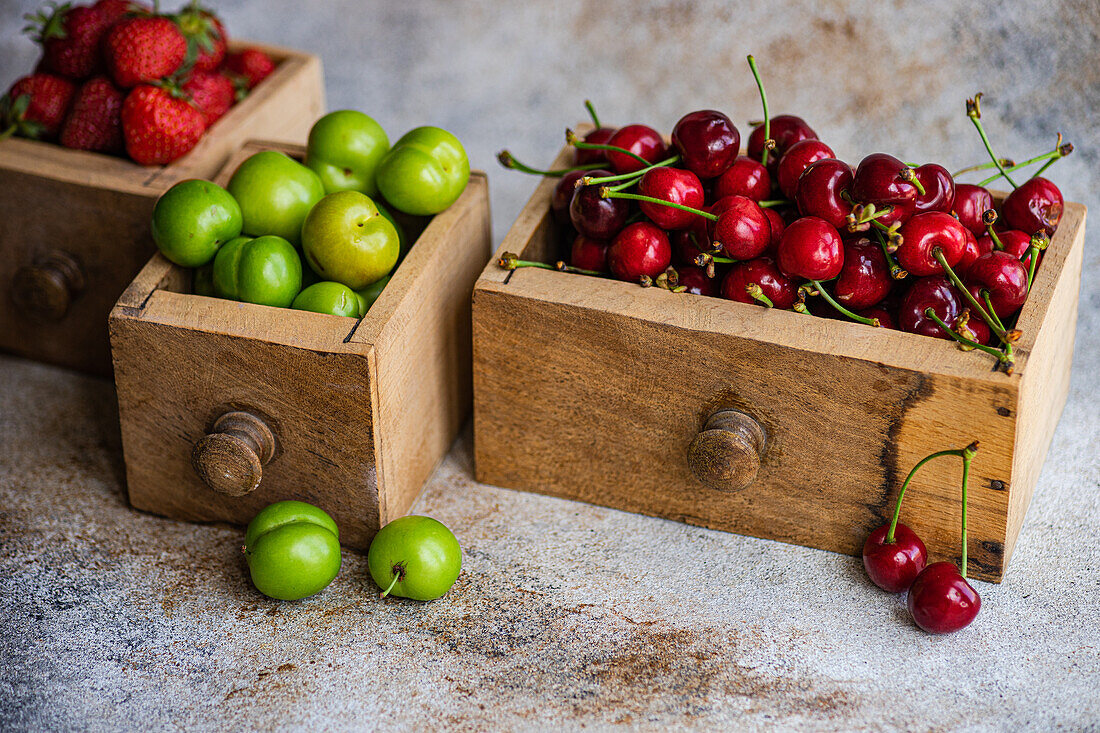 Eine verwitterte Holzschublade ist voll mit grünen Bio-Pflaumen, süßen Kirschen und reifen Erdbeeren, die einen rustikalen und natürlichen Charme versprühen