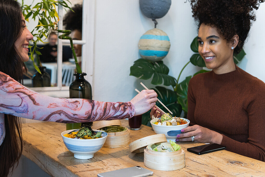 Seitenansicht von verschiedenen Freundinnen, die am Tisch sitzen und leckere Pastete essen, während sie ein Wochenende im Restaurant verbringen