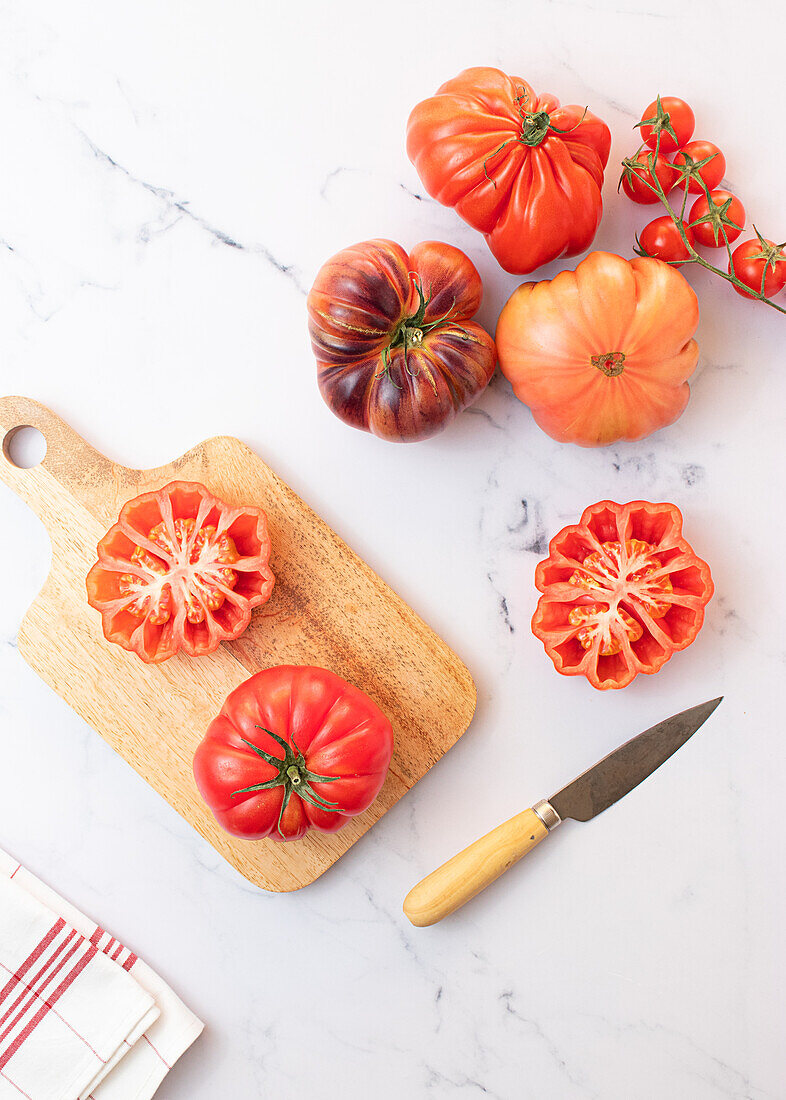 Tomatensalatzubereitung von oben auf einem Holzbrett mit einem Messer und einer Auswahl von Tomaten