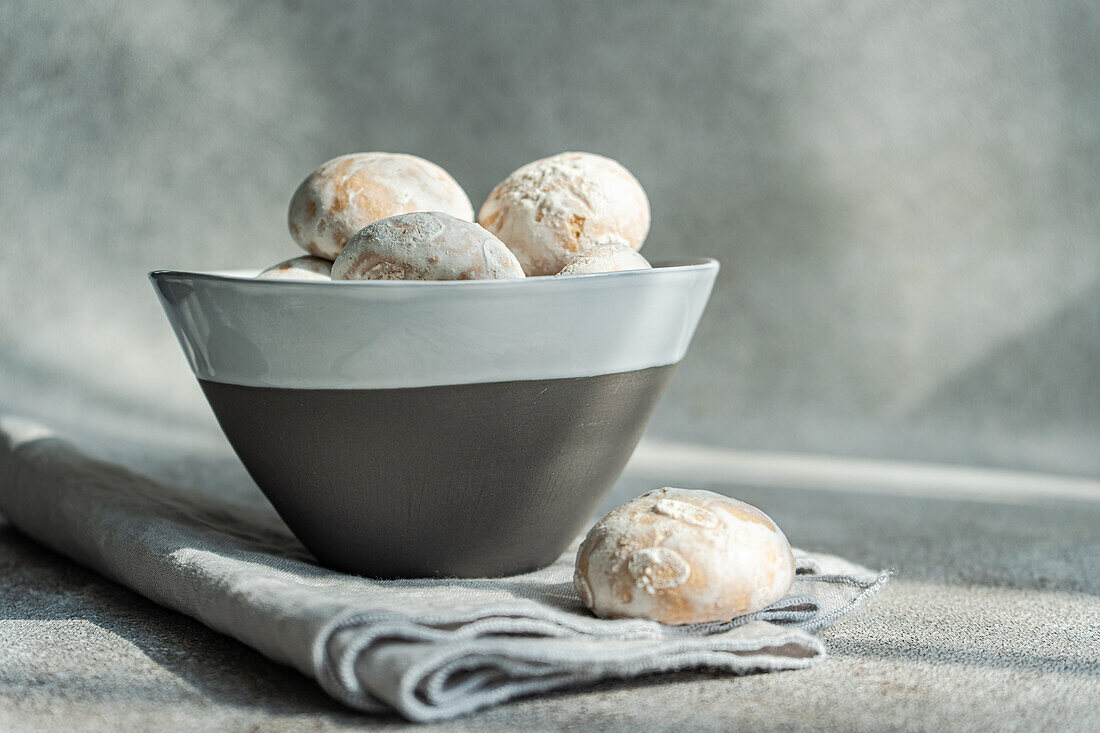 A modern grey bowl filled with powdered sugar-coated cookies on a textured linen, with soft lighting enhancing the cozy atmosphere