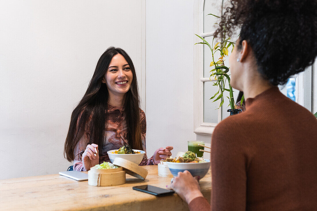 Side view of diverse female friends sitting at table and eating tasty poke while spending weekend in restaurant