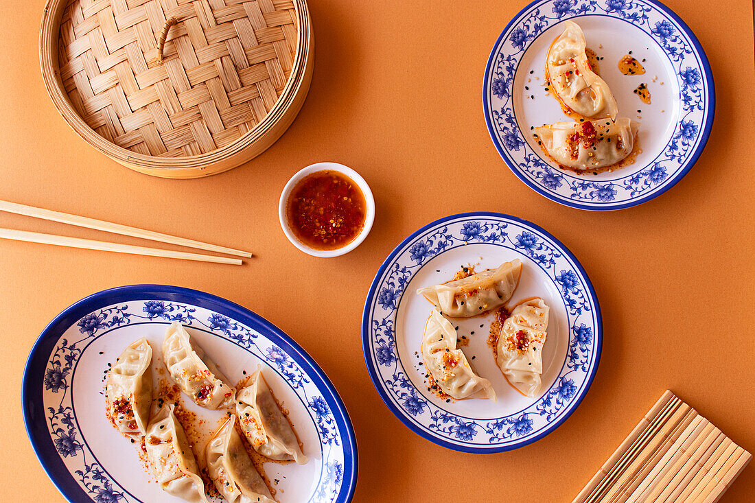 Chinesische Teigtaschen, gedünstet und gebraten, kunstvoll arrangiert auf blau-weiß gemusterten Porzellantellern, ergänzt durch einen Bambusdampfgarer und eine Dip-Sauce - perfekt für kulinarische Themen