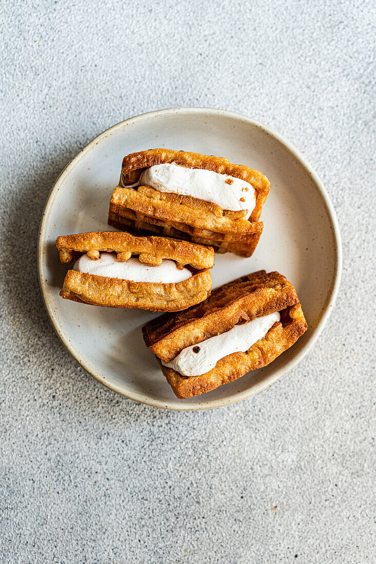 Stack of golden homemade waffles with creamy vanilla marshmallow filling served on a ceramic plate with a textured background