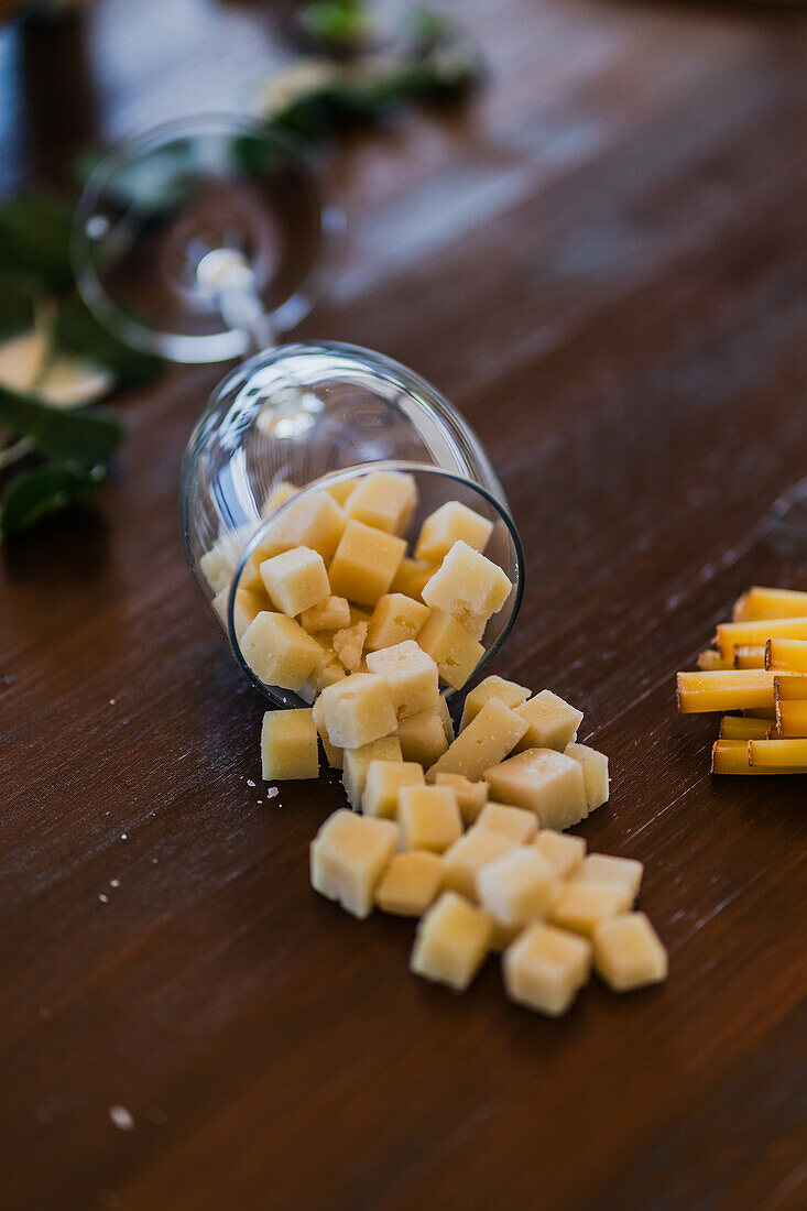 Verschüttete Käsewürfel aus einem umgekippten Weinglas auf einem Holztisch