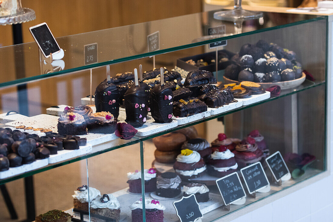 Assorted tasty vegan desserts placed on glass shelves of showcase in bright bakery