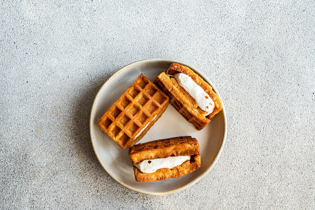 Frische hausgemachte Waffeln, gefüllt mit flauschigem Vanille-Marshmallow, serviert auf einem Keramikteller, Draufsicht auf einen strukturierten Hintergrund