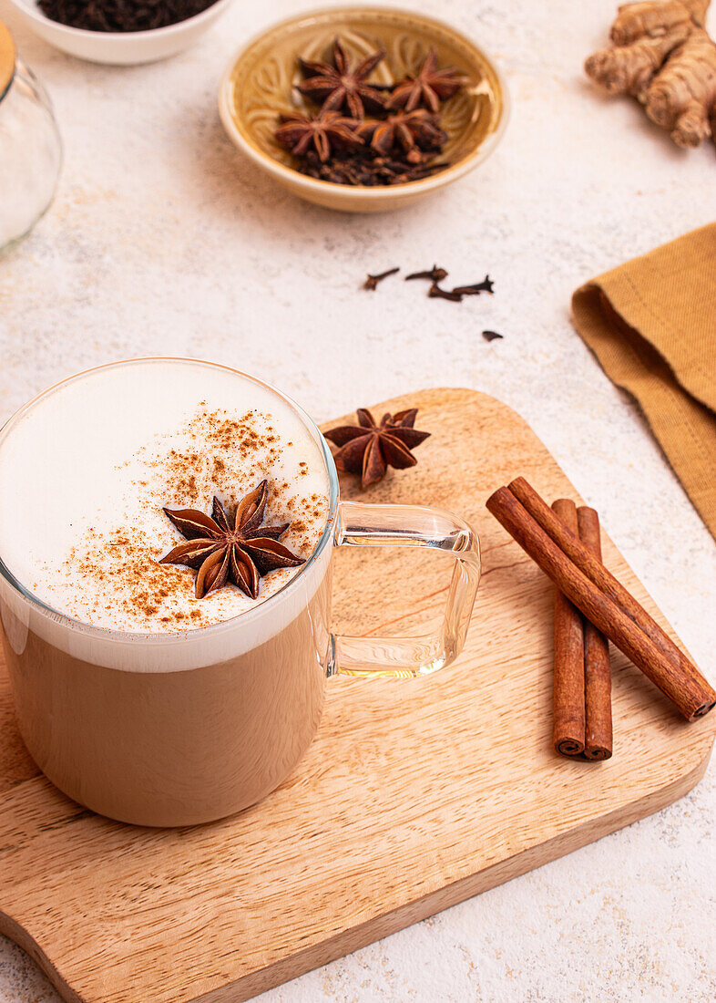 Von oben: Eine dampfende Tasse Chai Latte mit Sternanis und Zimt bestreut auf einem Holzbrett im rustikalen Stil