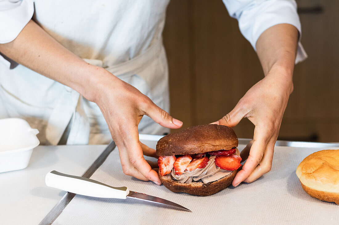 Unbekannte Bäckerin hält süßen veganen Biskuitkuchen mit Schlagsahne und Erdbeeren in einer Bäckerei