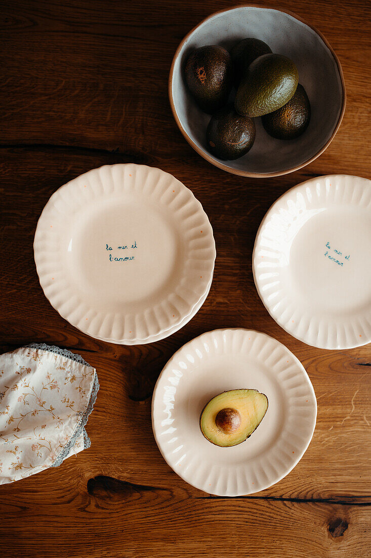 An artistic top-down view of ripe avocados in a bowl and halved on plates with handwritten phrases on a wooden surface