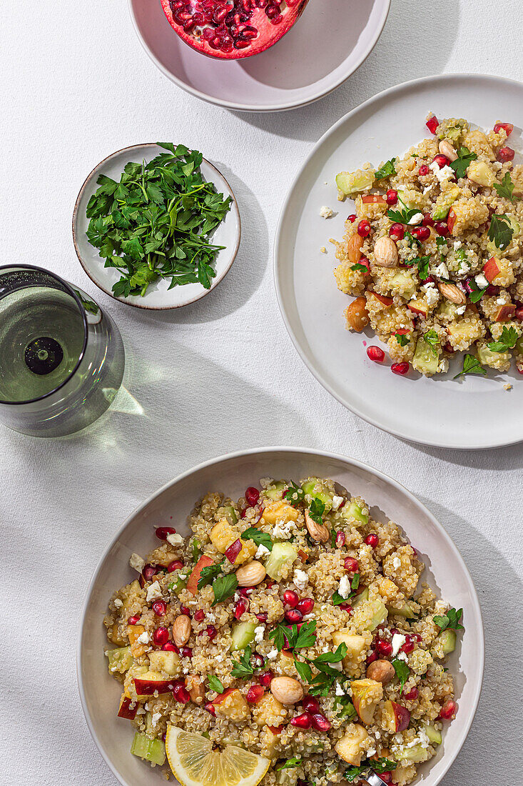 Blick von oben auf zwei Schalen mit buntem Quinoa-Salat, garniert mit Granatapfelkernen, Nüssen und Kräutern.