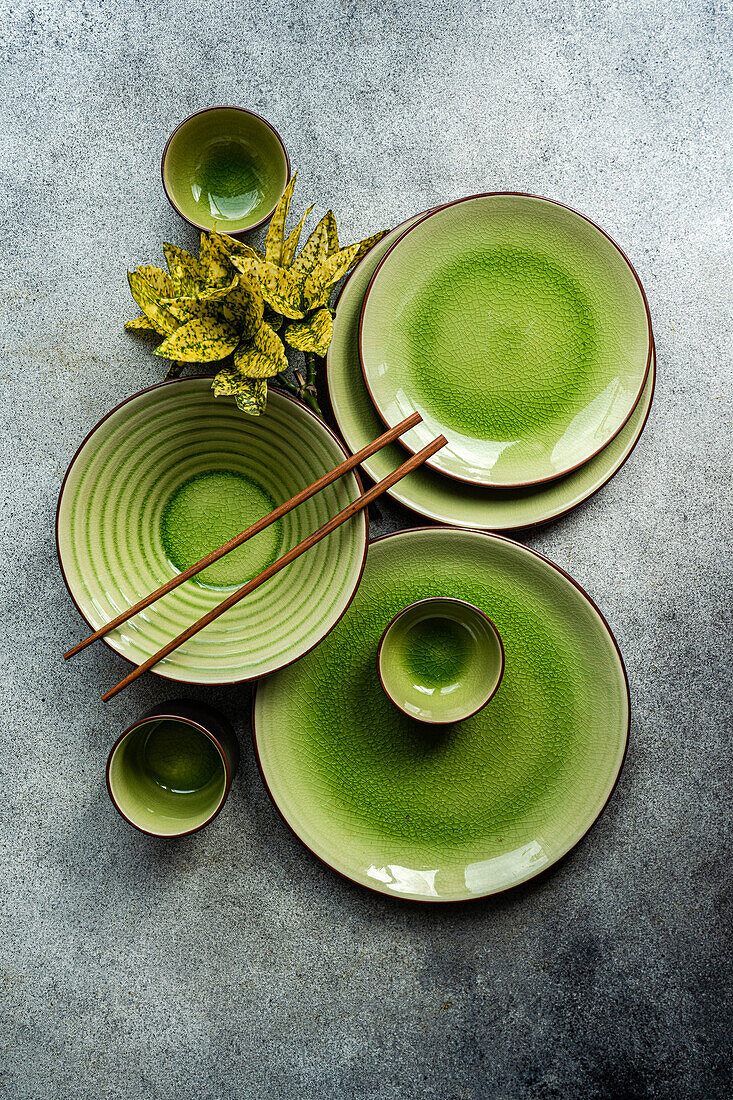 Top view of an elegant table setting featuring bright green ceramic dinnerware and wooden cutlery on a textured grey surface.