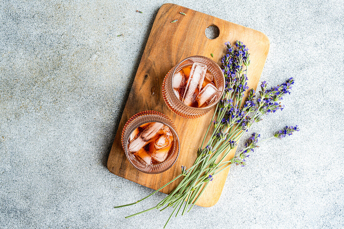 Two glasses of iced cognac cocktail beautifully presented with sprigs of lavender on a rustic wooden cutting board, showcasing an elegant and aromatic drink setup