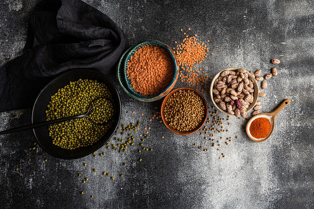 An array of raw beans and lentils displayed elegantly on a dark, textured background Includes various bean types, colors, and textures, paired with spices