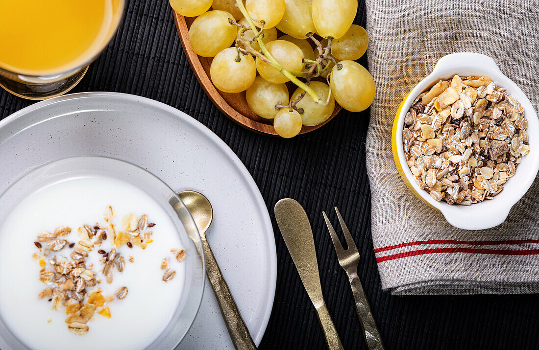 Top view of a well-balanced breakfast featuring a bowl of cereals with yogurt, fresh grapes, and a glass of orange juice, all neatly arranged on a textured table.