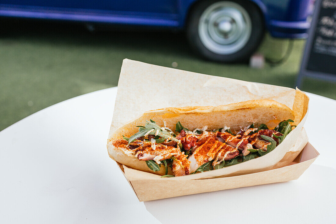 Delicious gourmet chicken sandwich with fresh arugula and spices, served in a paper tray at a trendy food truck gathering