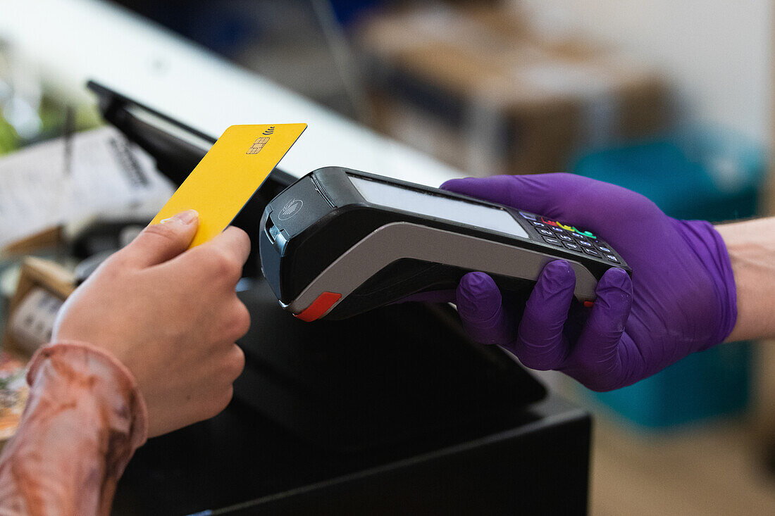 Unbekannte Frau mit Plastikkarte beim Bezahlen am POS-Terminal in einem Café