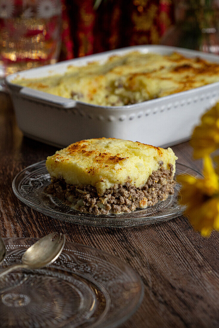 Homemade meat pie topped with golden brown mashed potatoes, served on a rustic wooden table.