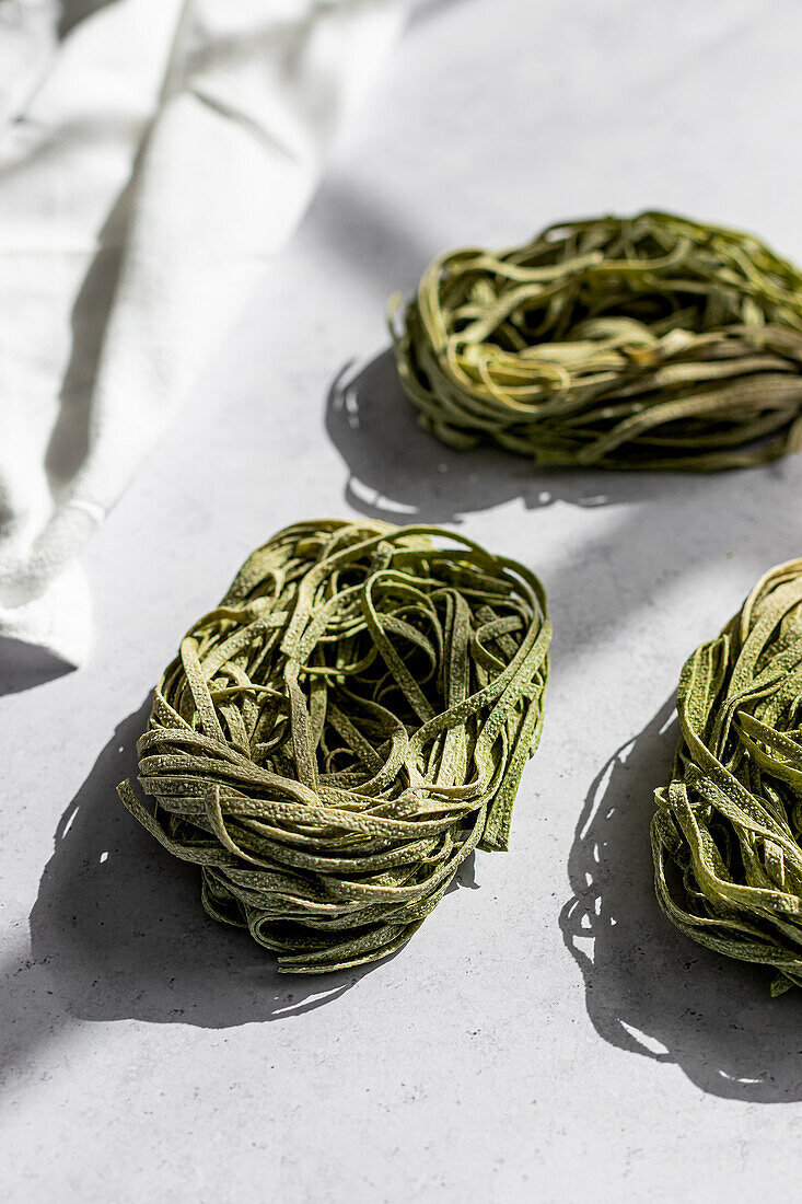 Elegant green pasta nests arranged neatly on a white surface with subtle shadow detail, illuminated by natural light