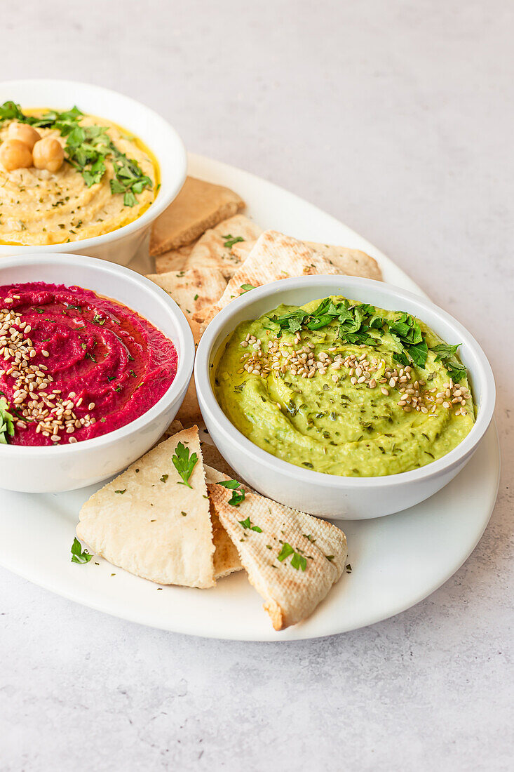 Assorted hummus varieties including classic, beet, and avocado served with pita bread on a white plate.