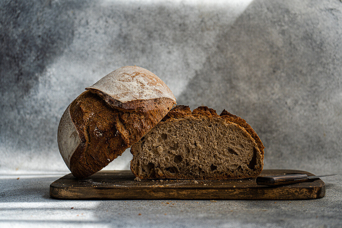 A rustic loaf of rye sourdough bread, freshly baked and sliced on a wooden cutting board, with a knife alongside