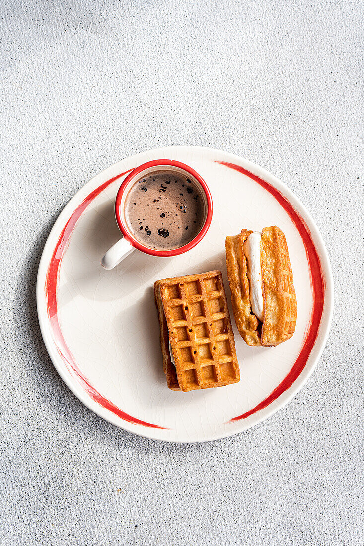 A plated breakfast of waffles with creamy vanilla marshmallow between them, paired with a cup of hot cocoa