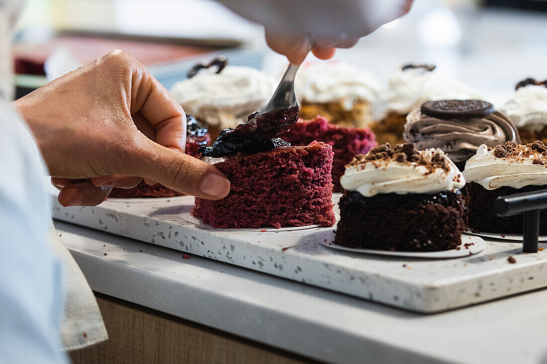 Anonymer Bäcker bestreicht Biskuitkuchen mit Beerenmarmelade, während er in einer Bäckerei vegane Desserts zubereitet