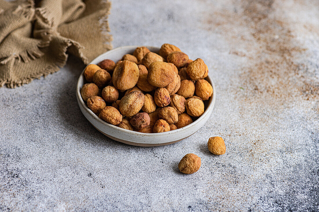 A bowl of Arashan Kandak, sun-dried apricots from Central Asia, on a textured surface with a burlap cloth